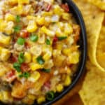 Overhead view of hot corn dip in black bowl surrounded by chips.