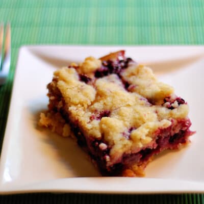 A serving of a blackberry pie bar on a square plate.
