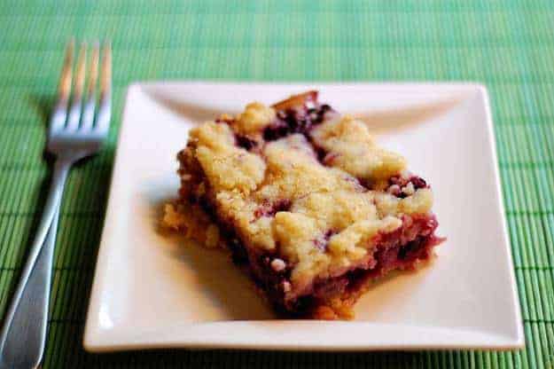 A serving of a blackberry pie bar on a square plate.