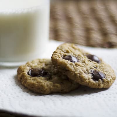 Two oatmeal cookies on a paper napkin in front of a glass of milk.