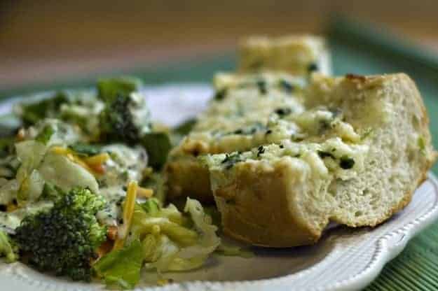 A piece of garlic bread on a plate with salad