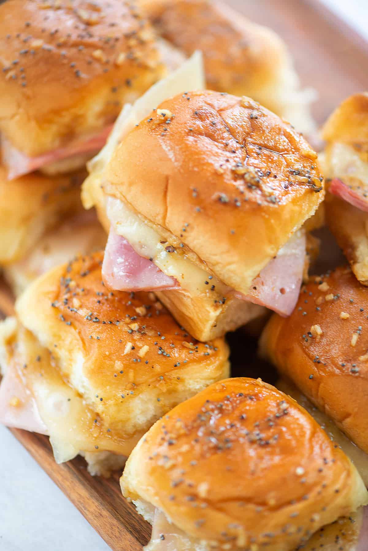 pile of ham and chees sliders on wooden board.