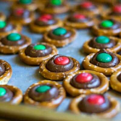 A bunch of pretzel rings with melted chocolate and m&m's on a baking sheet.