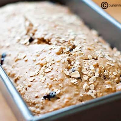 A loaf of bread topped with oats in a bread pan.