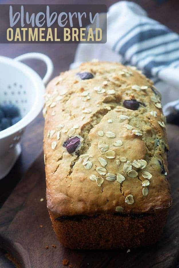 A loaf of bread on a cutting board with visible oats and blueberries.