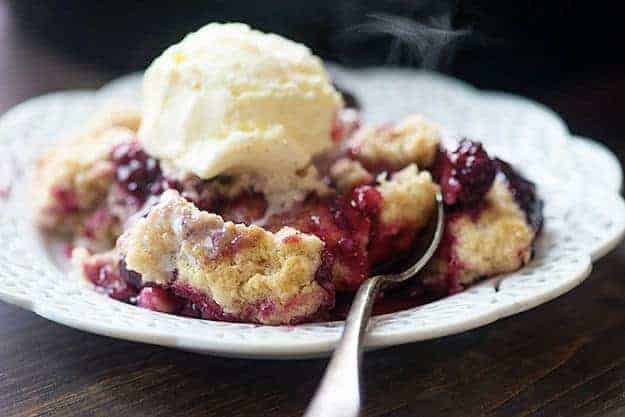 This blackberry cobbler recipe has quickly become our favorite way to make cobbler! The dough on top of the berries is just amazing! blackberry cobbler on white plate with ice cream
