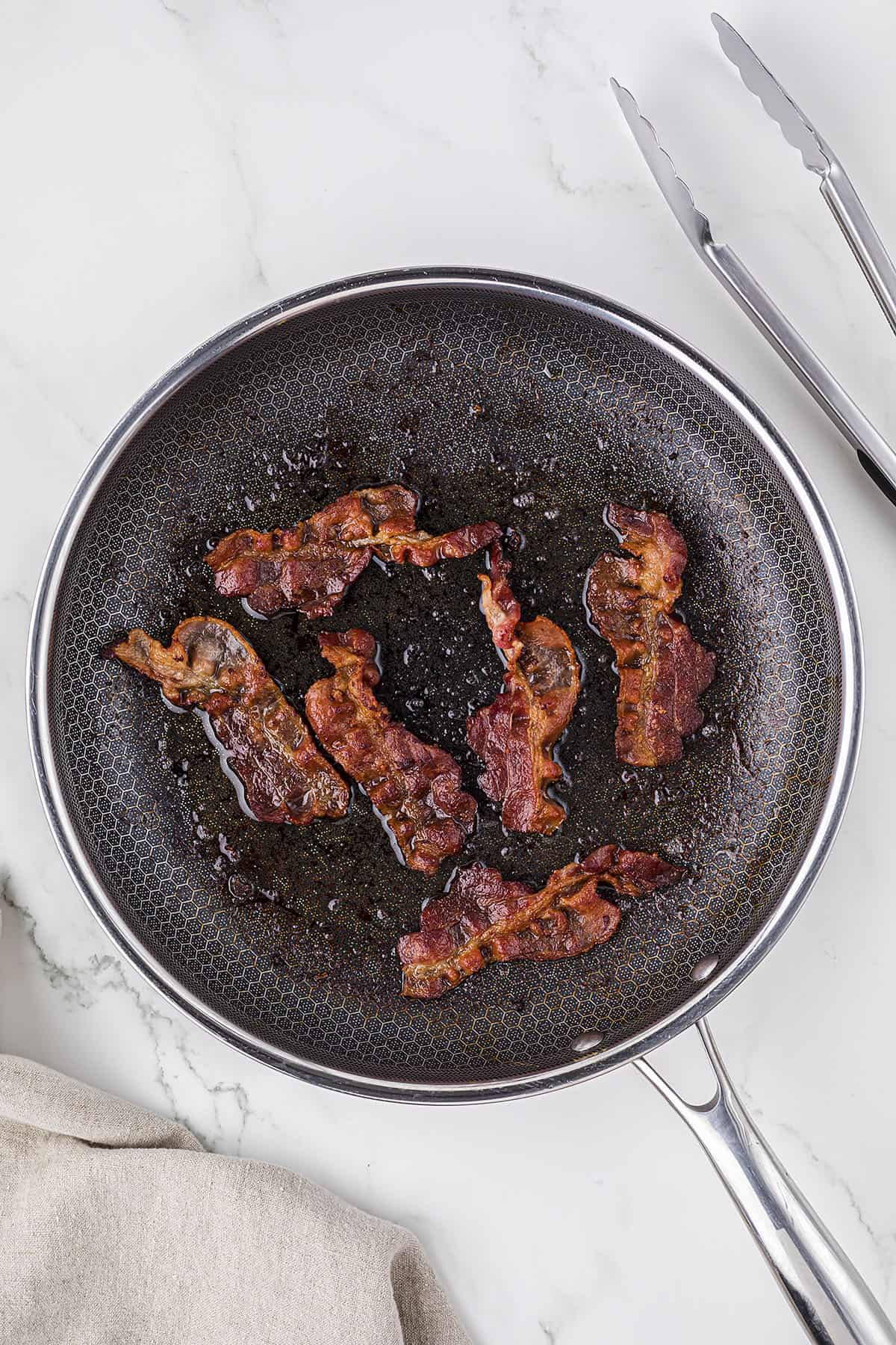 Bacon being fried in a skillet.