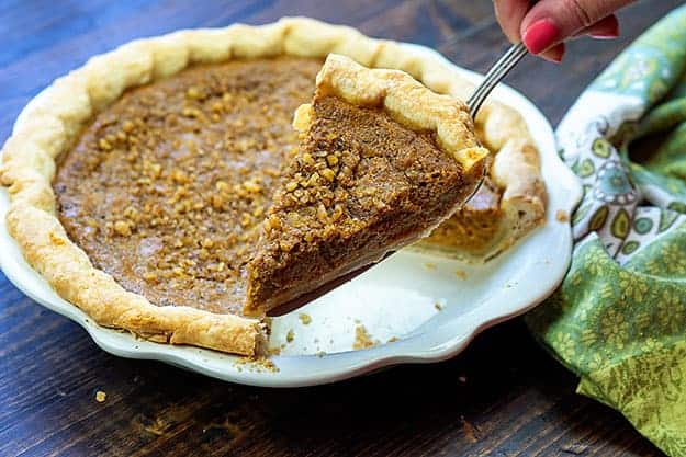 A piece of pumpkin pie being held up to the camera on a pie scoop.