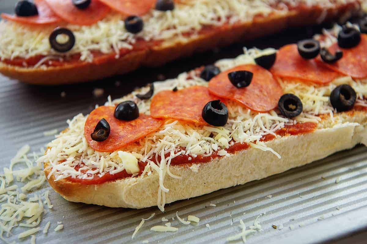cheese, pepperoni, and olives on loaf of bread.