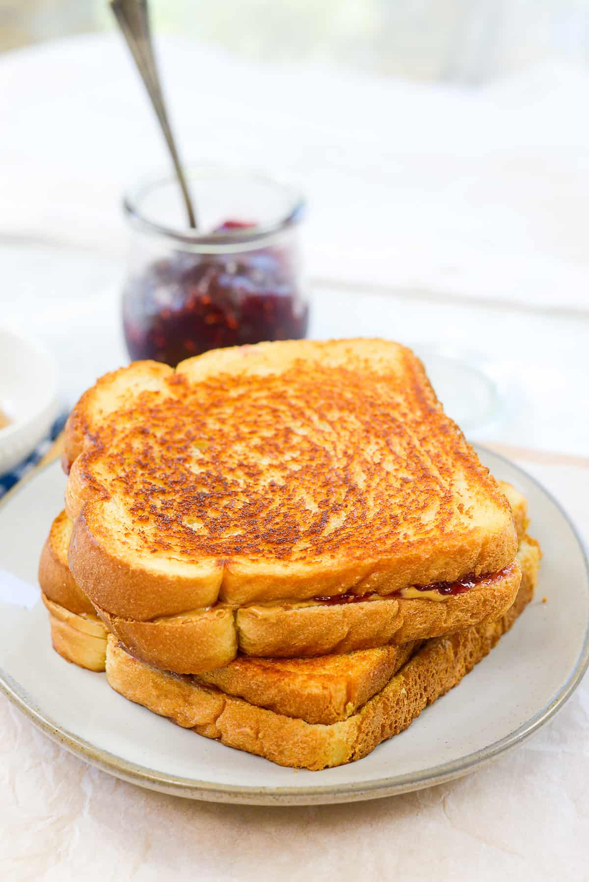 Stack of grilled peanut butter and jelly sandwiches on white plate.