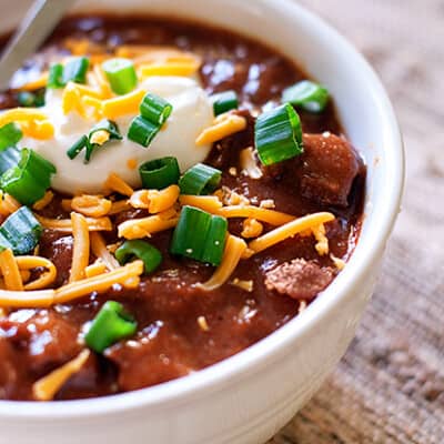 A closeup of a bowl of steak chili topped with chives and shredded cheddar