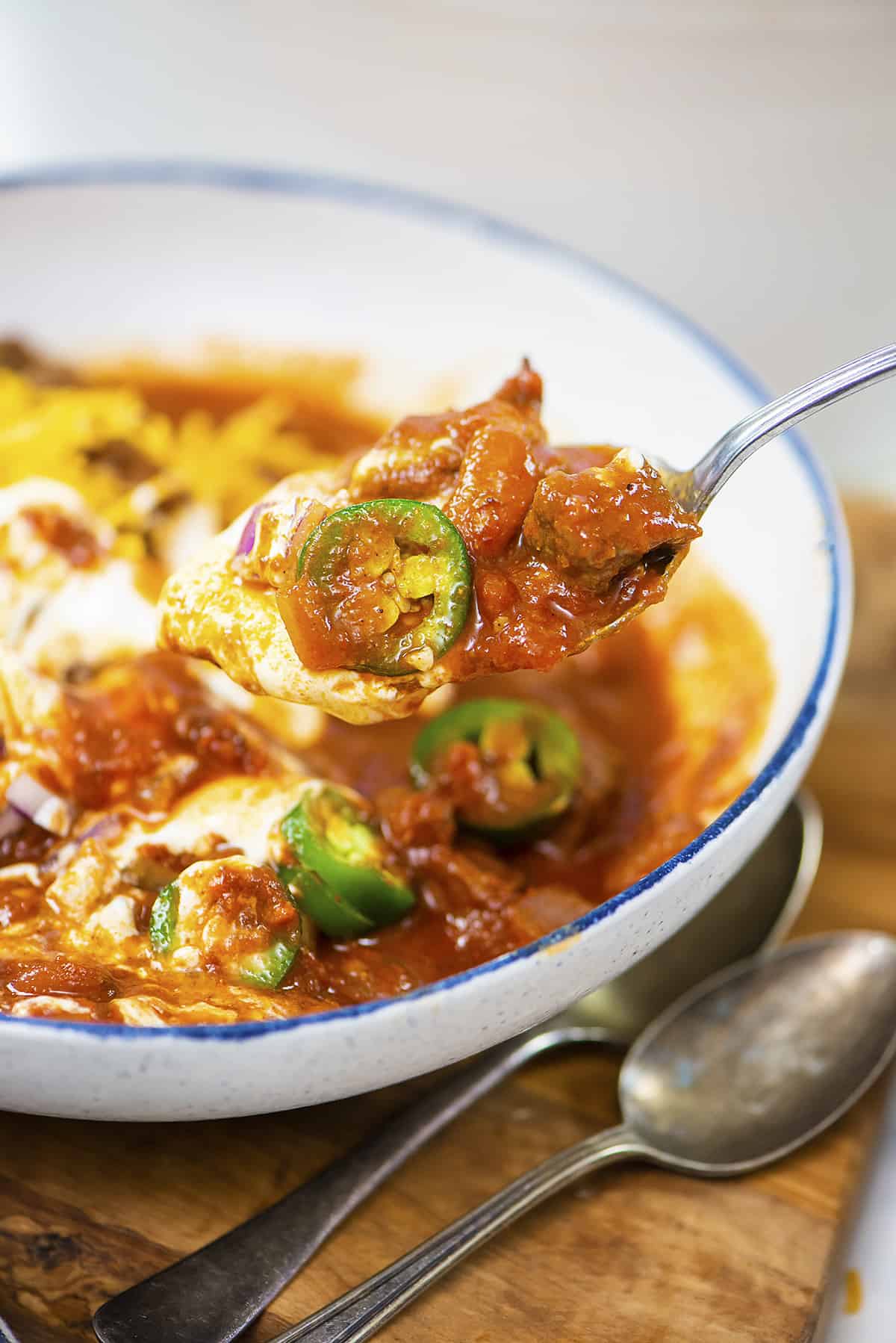 Spoon full of steak chili over bowl.