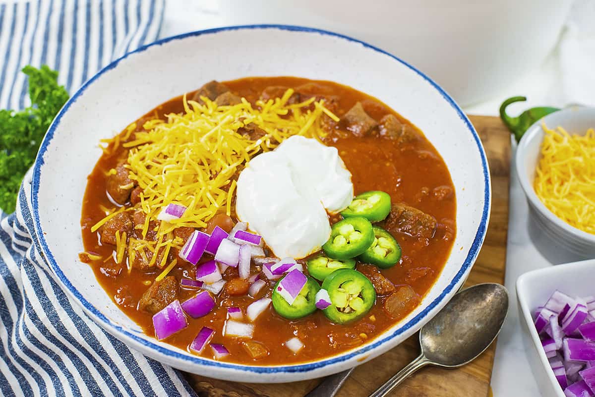 Steak chili in bowl topped with cheddar, sour cream, and onion.