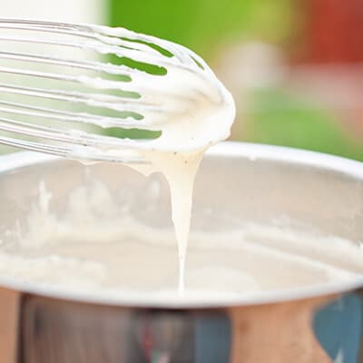 A close up of a whisk above a mixing bowl