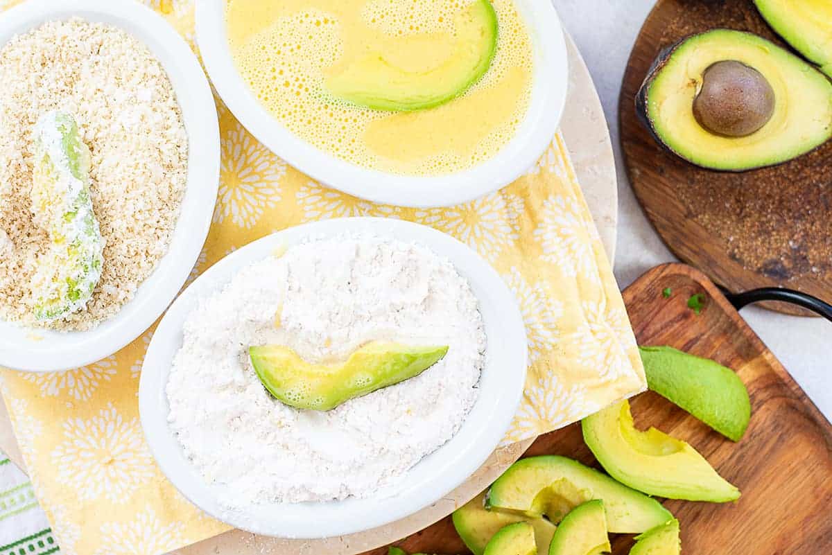 avocado slices being dipped in flour, egg, and panko.