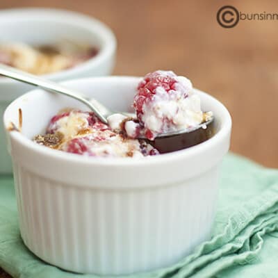 A close up of a cup of raspberry gratin with a spoon scooping out a raspberry