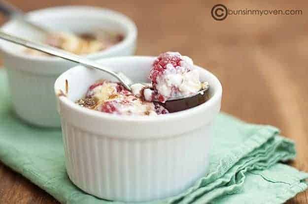 A close up of a cup of raspberry gratin with a spoon scooping out a raspberry