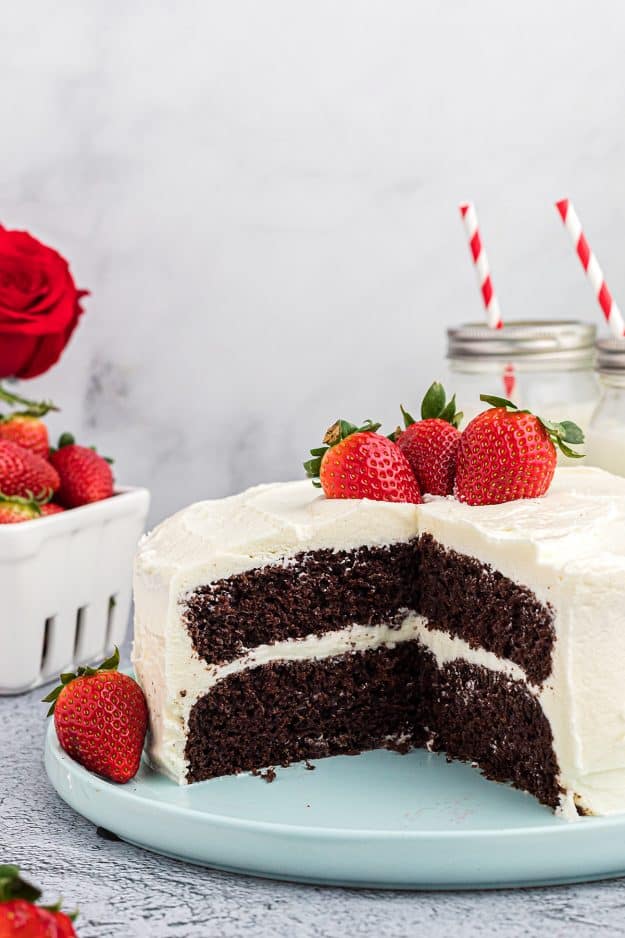 chocolate cake on cake plate with whipped frosting and berries.