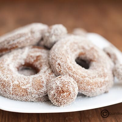 A close up of a few apple cider donuts on a plate.