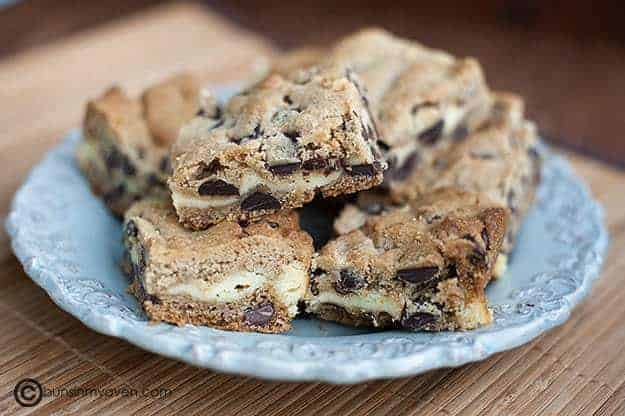 A plate with several chocolate chip cookie cheesecake bars on it.