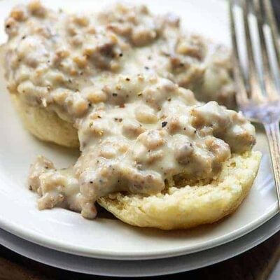 small white plate with a biscuit topped with sausage gravy.