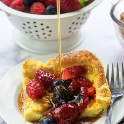 german pancake with fresh fruit and syrup on white plate