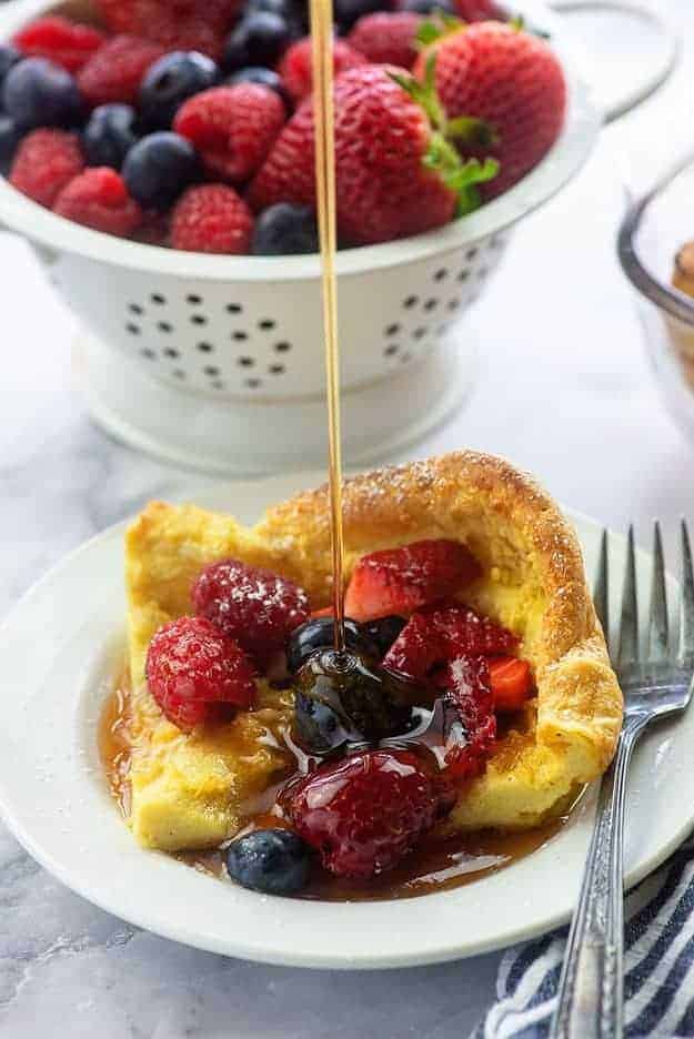 german pancake with fresh fruit and syrup on white plate