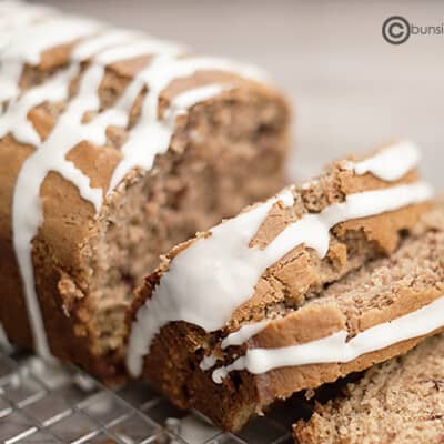 A loaf of maple cinnamon quick bread partially sliced on a cooling rack.