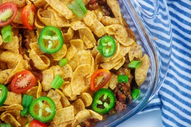 Frito chili pie in casserole dish topped with jalapenos and tomatoes.