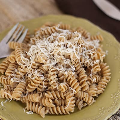 A plate of pasta salad topped with cheese and a fork.