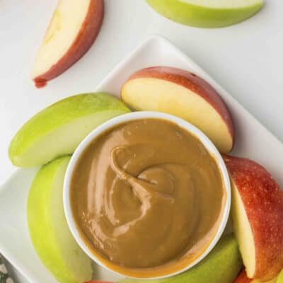 Dulce de leche in small white dish surrounded by apples.