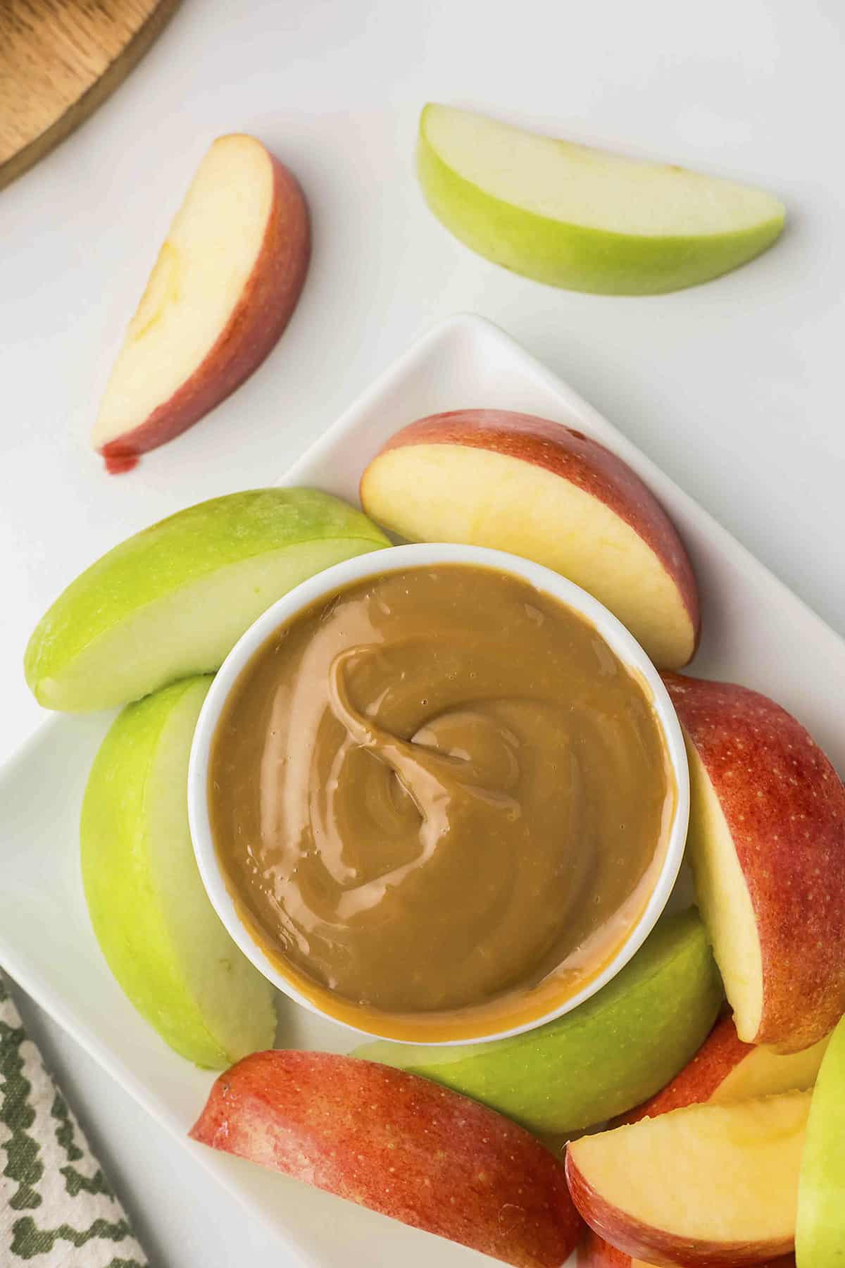 Dulce de leche in small white dish surrounded by apples.