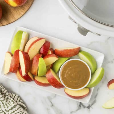 Dulce de leche in small white dish on platter with sliced apples.