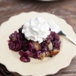 A blackberry cobbler topped with whipped cream on a white plate.