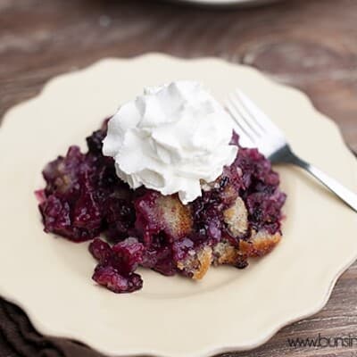A blackberry cobbler topped with whipped cream on a white plate.