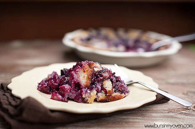 A serving of blackberry cobbler on a white plate in front of a cobbler pie.