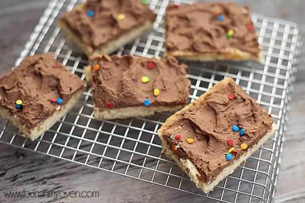 A closeup of a sugar cookie bar with chocolate frosting and sprinkles 