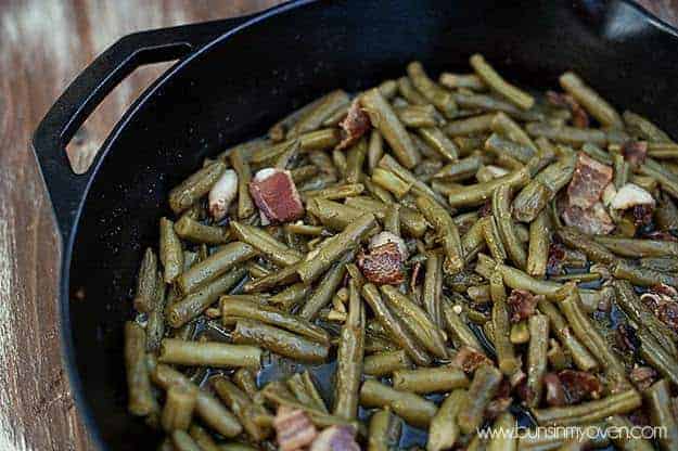 A closeup of green beans and bacon cooking in a cast iron skillet