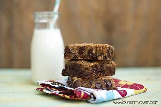 Three molten chocolate chip cookie bars stacked up in front of a jar of milk 