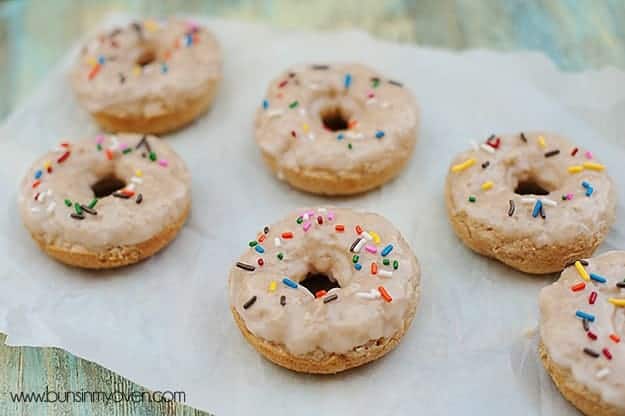 Several vanilla doughnuts topped with sprinkles on a  table.