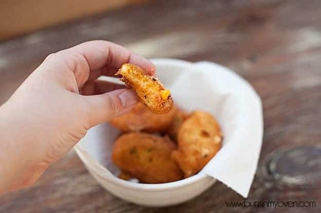 A person holding up a cheddar bite with a bite taken out of it.