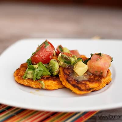 Corn cakes topped with tomato on a white plate