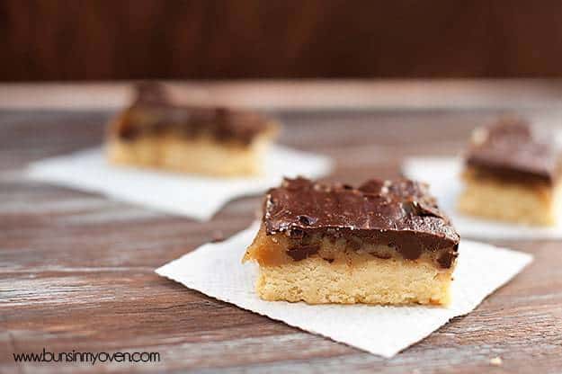 A close up of a chocolate caramel shortbread bar on a white napkin. 