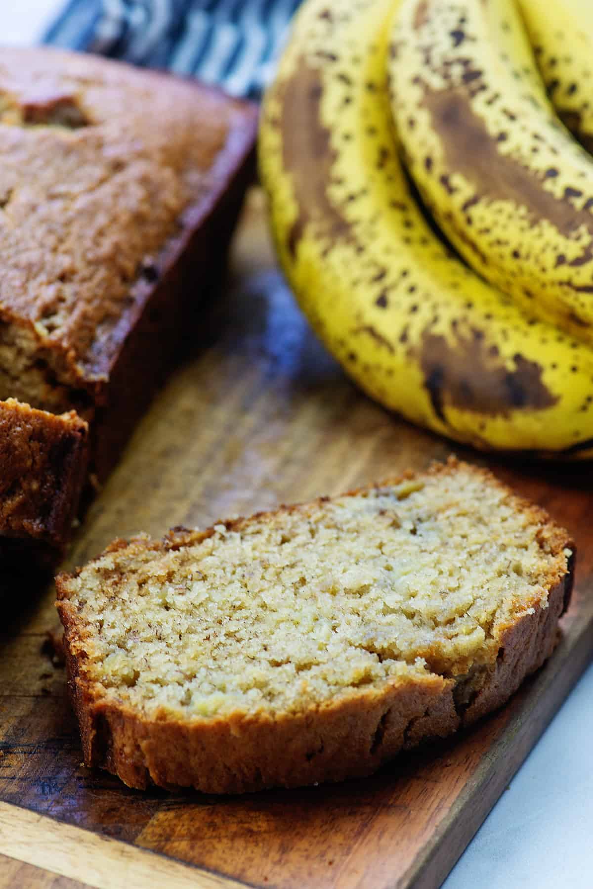 sliced banana bread on wooden cutting board next to ripe bananas