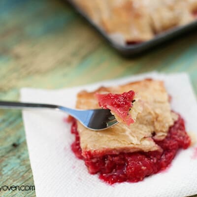A fork with raspberry on it resting on top of a serving of raspberry slab pie.