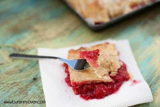 A fork with raspberry on it resting on top of a serving of raspberry slab pie.