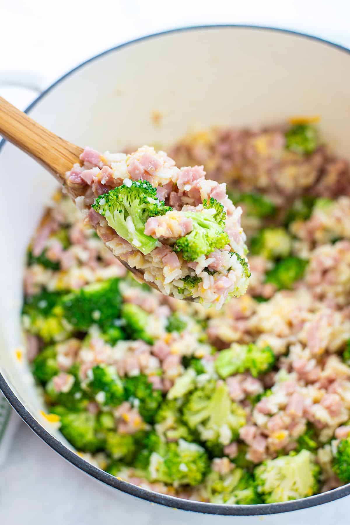 wooden spoon full of rice, ham, and broccoli over pot.