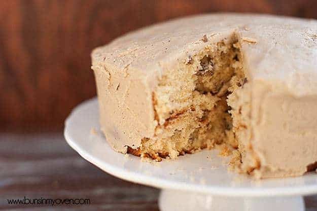 A butter pecan cake on a cake stand with a piece cut out of it