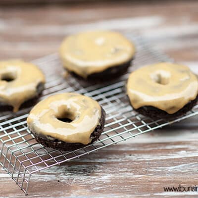 Four donuts with peanut butter icing on a cooling wire rack.