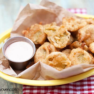 A close up of an appetizer basket with fried pickles and ranch dressing in it.